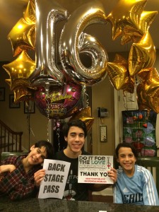 Michael smiling with his brother and sister. Sitting under huge #16 balloons holding a back stage pass.