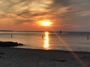 sunset at marthas vineyard. Gold and orange colors in the sky and a beam of light acrosst the water to the rocky beach