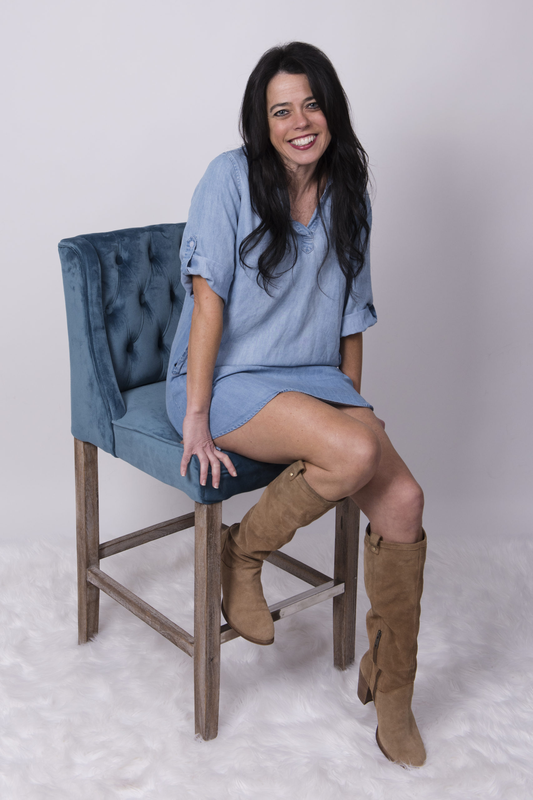 Kristin sitting on a blue chair in a blue dress with a white background