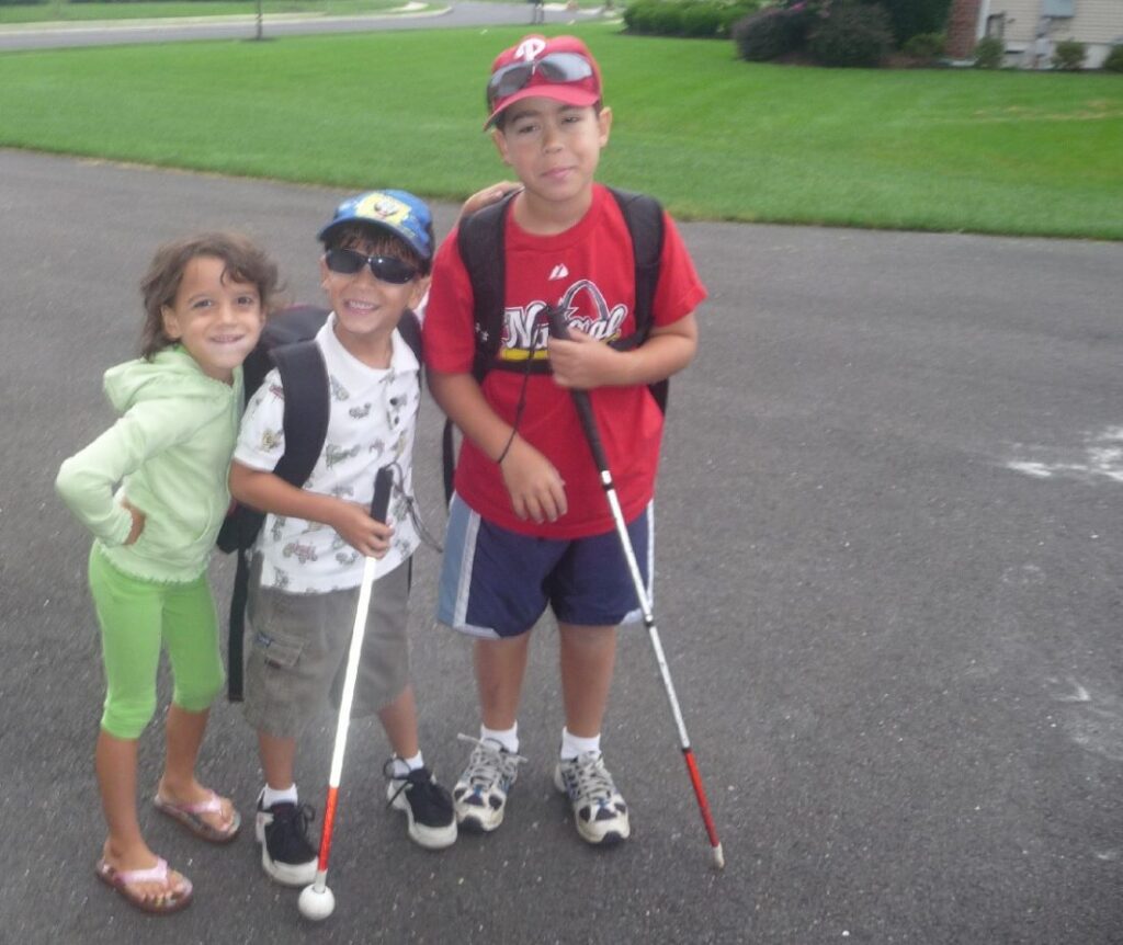 Kristin’s sons Michael and Mitchell as young boys holding their white canes, with their sister