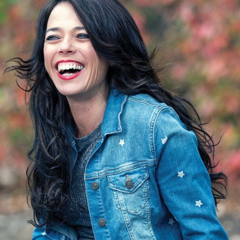 Kristin Smedley laughing in a denim jacket, with autumn leaves behind her